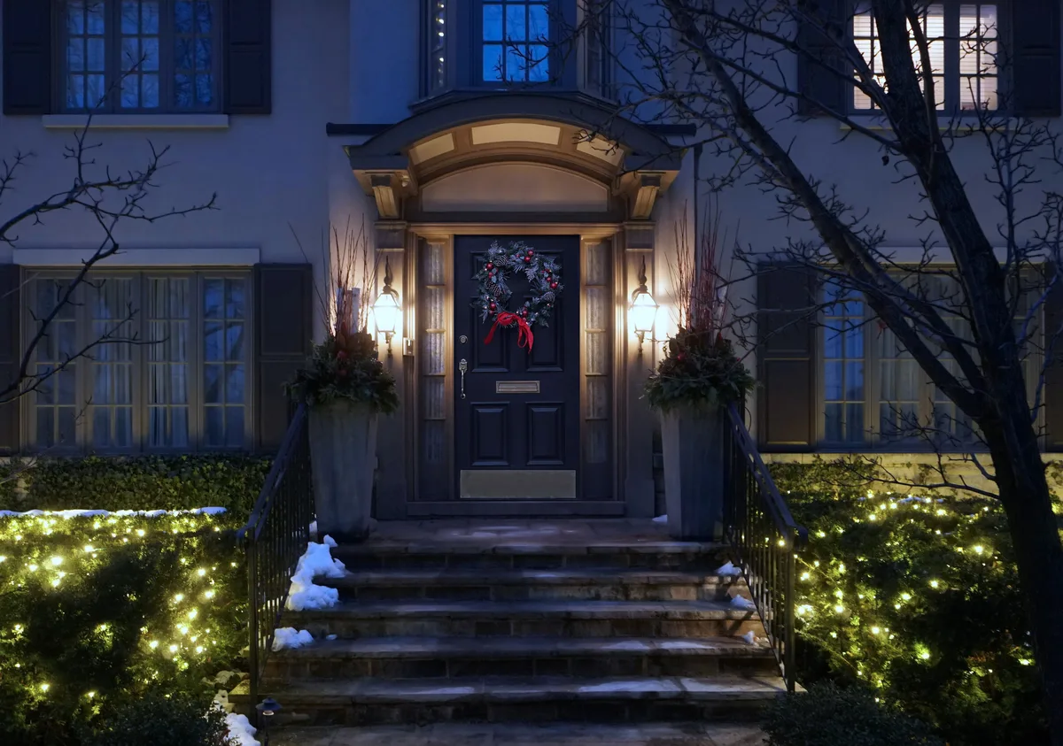 Townhouse entrance at dusk with a wreath on the door and lit garlands along the steps