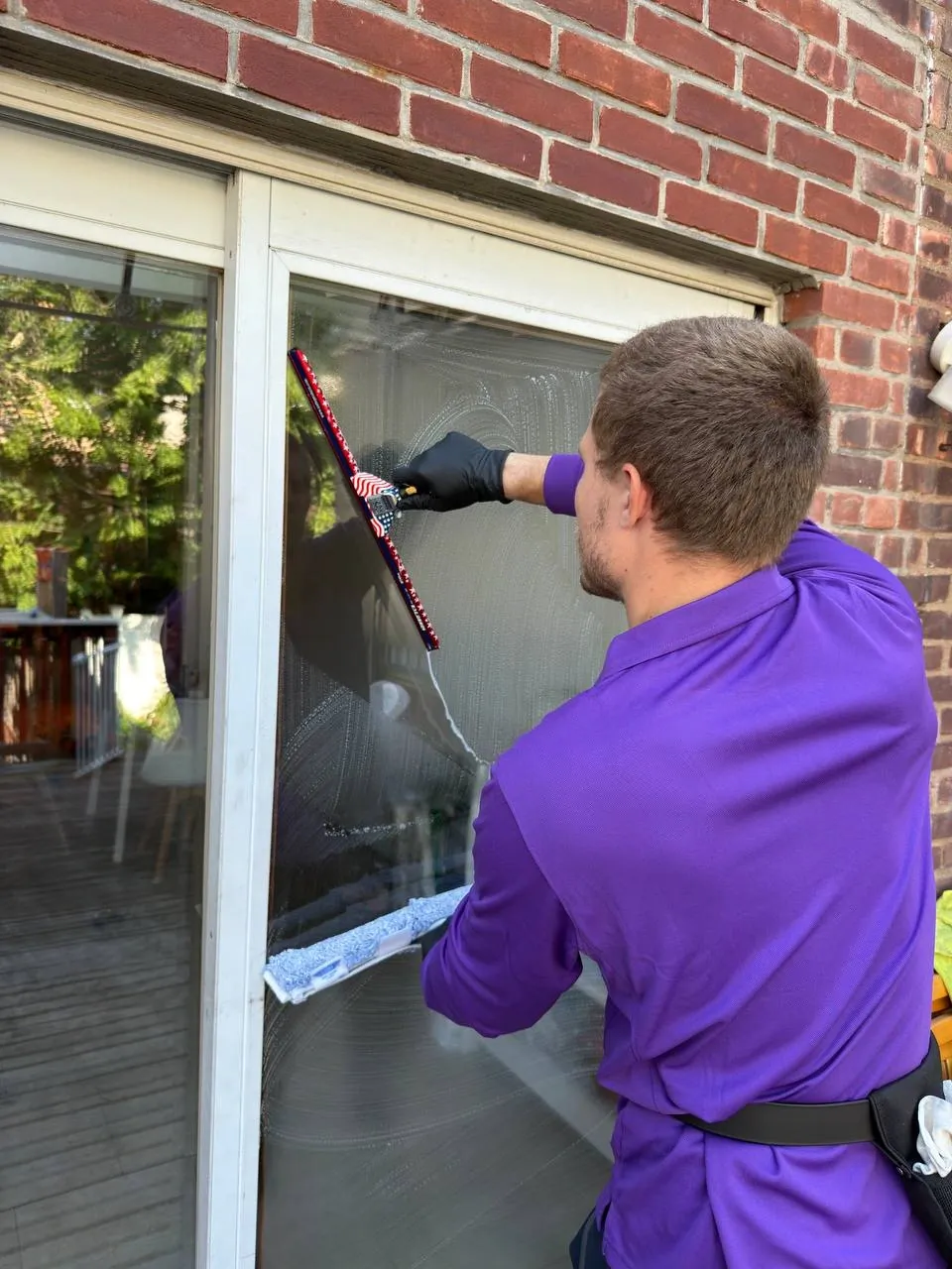 Purple Window Cleaning technician washing a residential window with a squeegee and washer