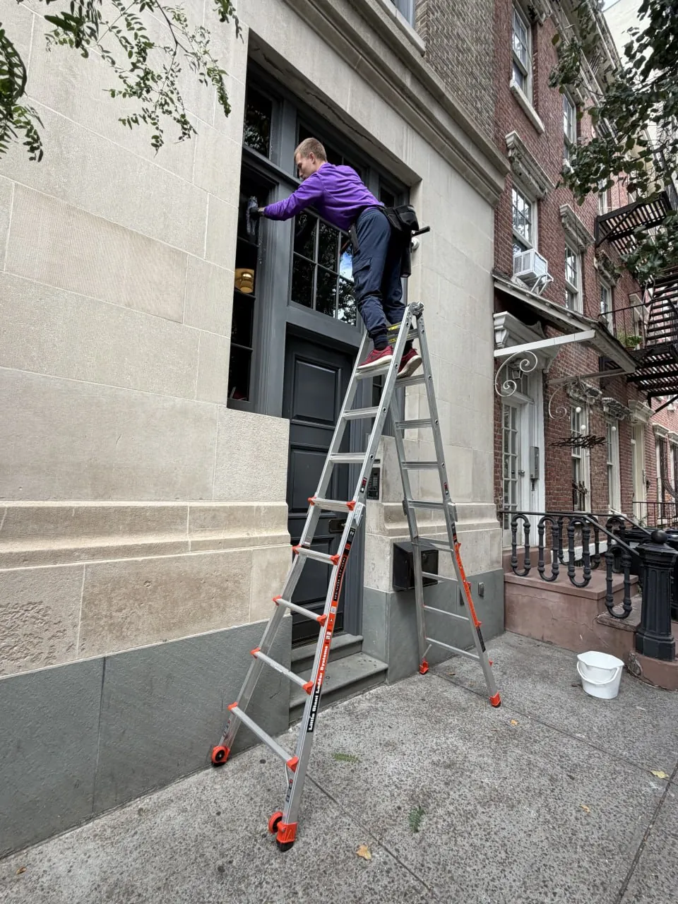 Purple Window Cleaning technician on a ladder cleaning the glass entry door of a Manhattan brownstone