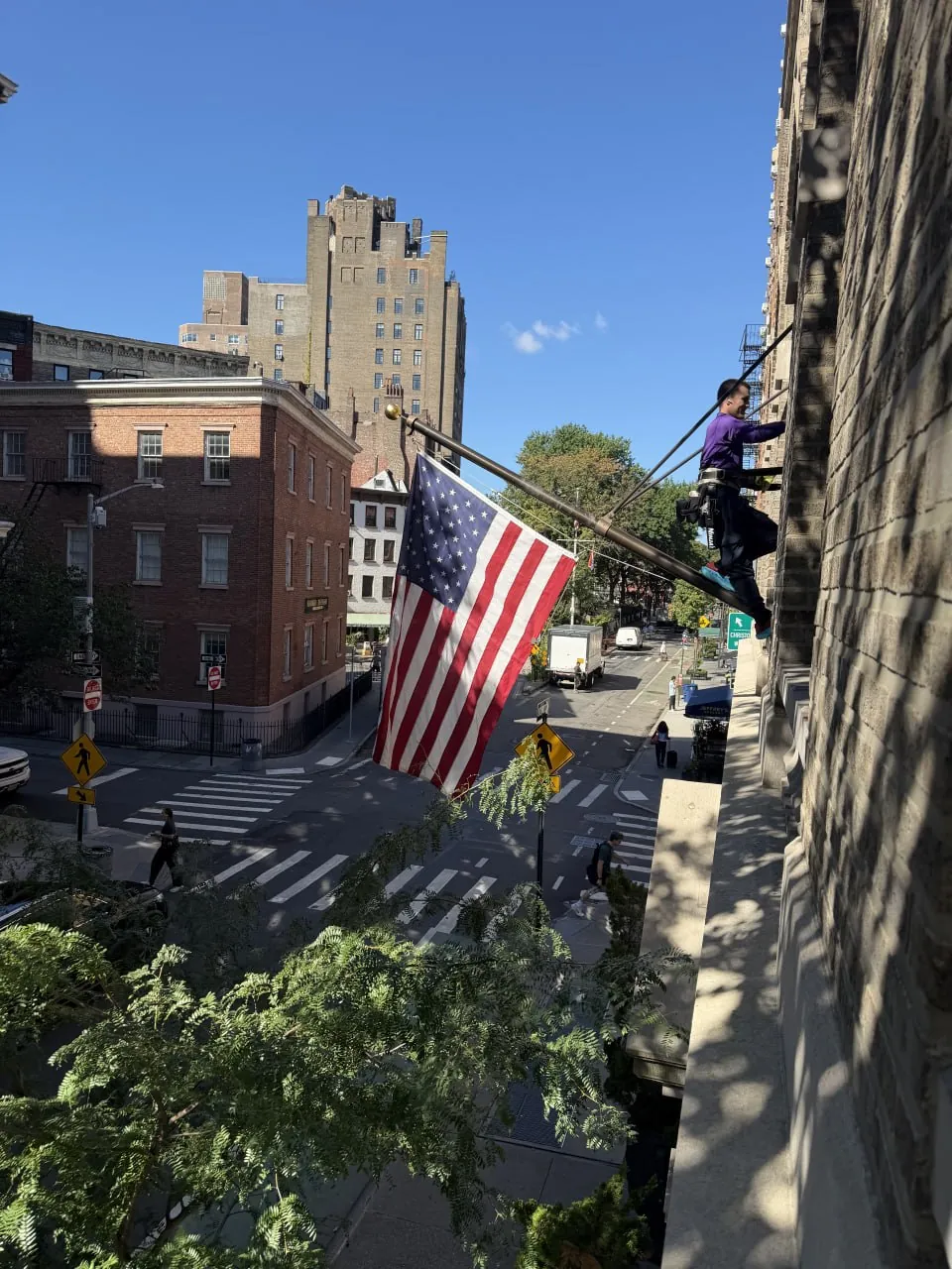 Purple Window Cleaning technician on a window ledge cleaning exterior windows above a New York City street