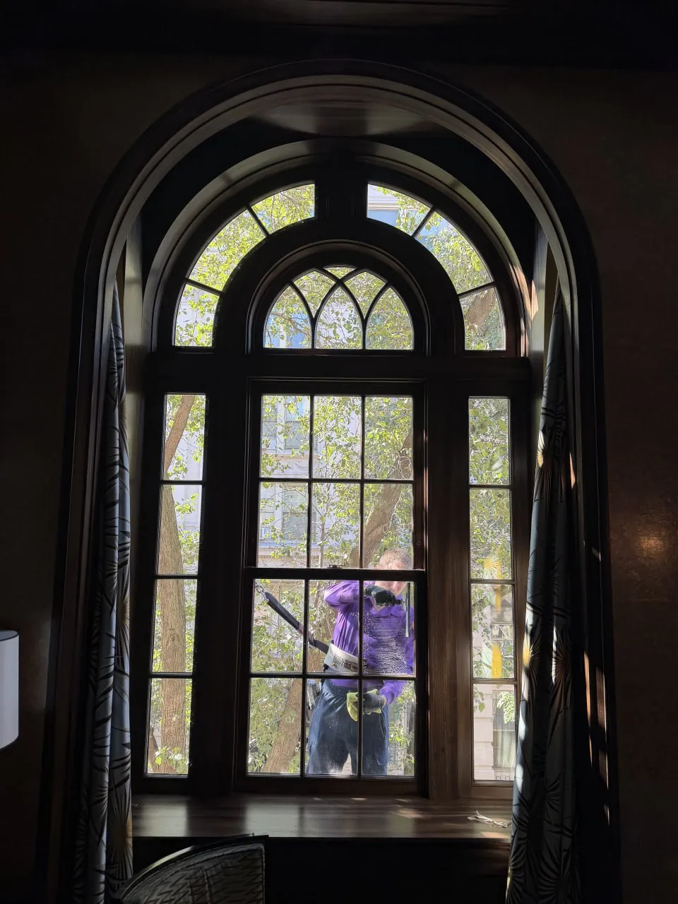 Arched townhouse window seen from inside while a Purple Window Cleaning technician cleans it from the outside