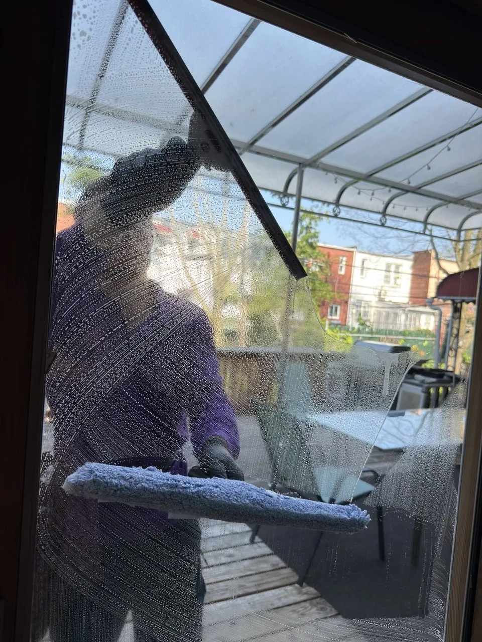 Purple Window Cleaning technician cleaning a residential patio door, seen from inside through the wet glass