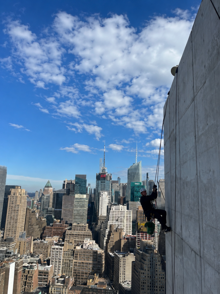 Rope access technician rappelling down a Manhattan high-rise facade above the Midtown skyline