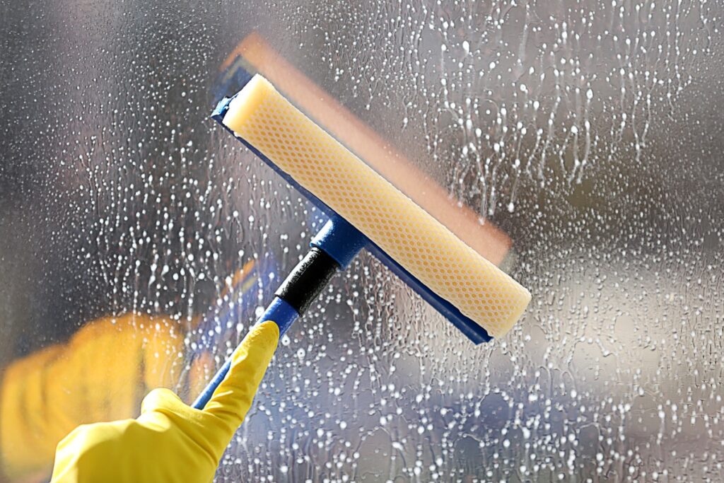 Close-up of a squeegee cleaning a soapy window